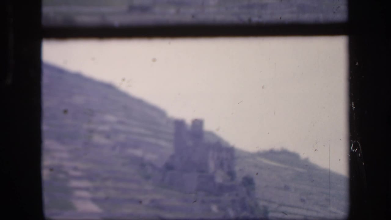 1949 Ireland home-movie frame showing terraced farmland and a weathered stone structure through a dark window frame.