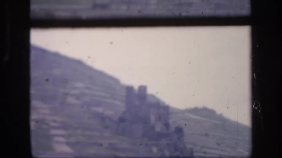 1949 Ireland home-movie frame showing terraced farmland and a weathered stone structure through a dark window frame.