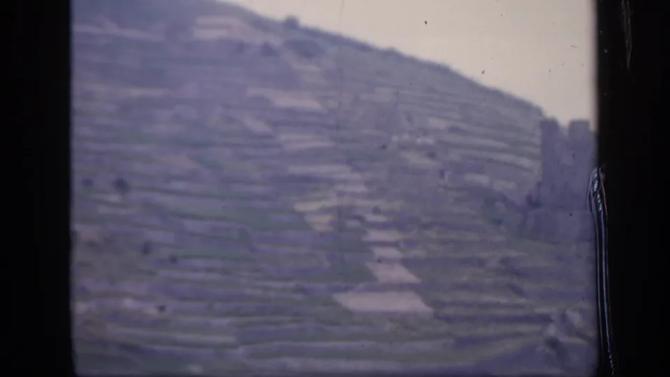 1949 Ireland frame of terraced hillside farmland with a weathered stone structure at the right edge and cloudy sky above.