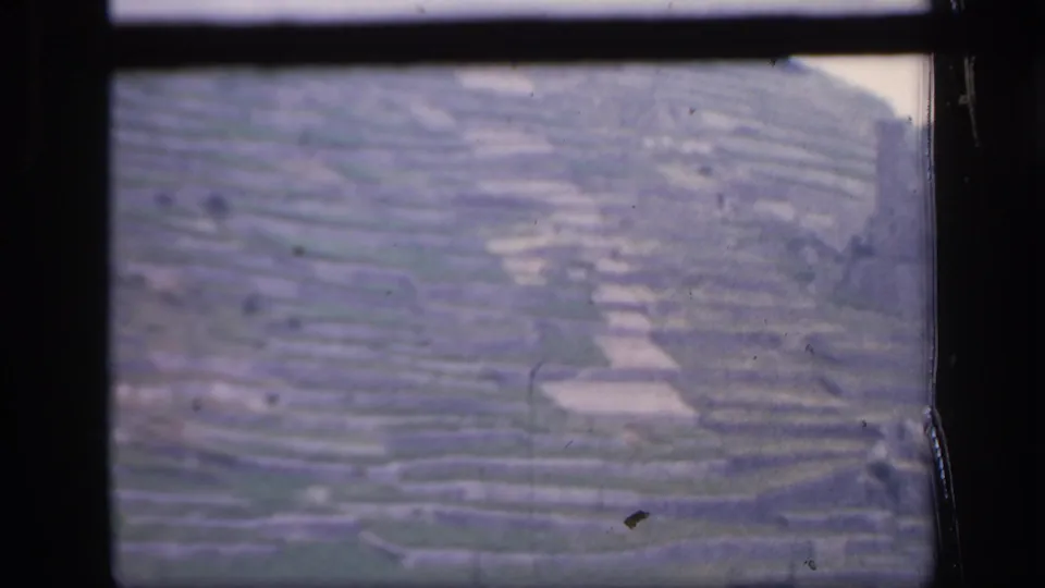 1949 Ireland home-movie frame of layered hillside farmland, pale field patches, and visible 8mm frame edges.