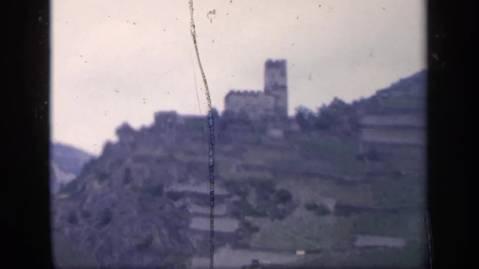 1949 Ireland 8mm frame with a distant stone tower-like building on a hillside above terraced fields.
