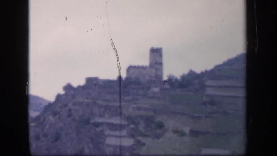 1949 Ireland home-movie frame showing a distant stone structure, hillside terraces, trees, and visible film scratches.