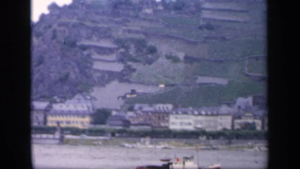 A 1949 Ireland riverside or seaside town view with terraced hillside, waterfront buildings and a small boat in the foreground.
