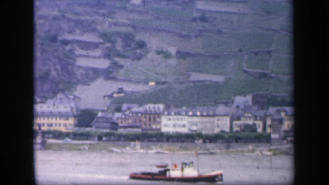 Small boat on a river below a town and terraced green hillside.
