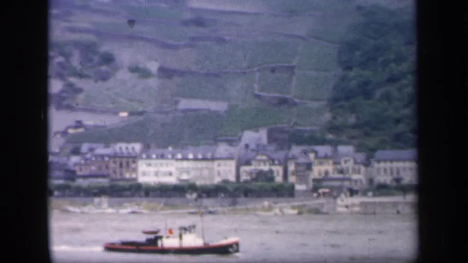Distant 1949 Ireland riverfront view with a small boat, town buildings, and cultivated-looking hillside terraces.