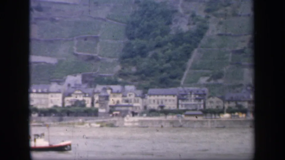 1949 Ireland 8mm view across water toward riverside buildings, terraced hills, and a partly cropped boat.