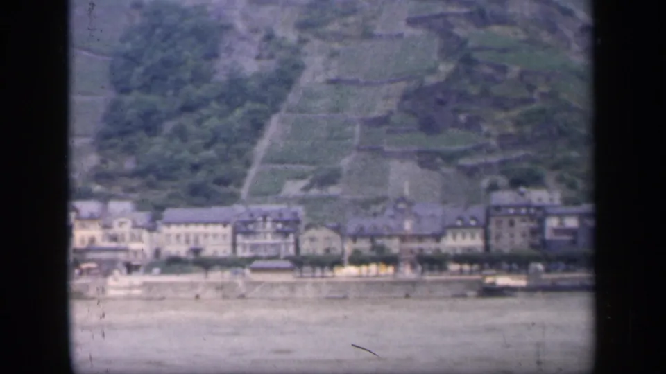 Final 1949 Ireland river town frame showing waterfront buildings, a broad water foreground, and terraced green hillside above.