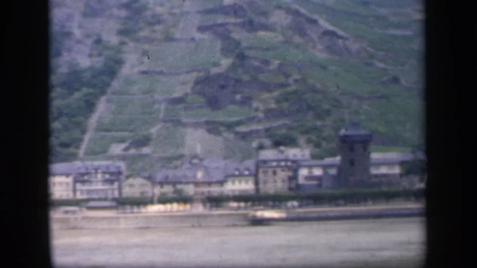1949 8mm home-movie frame showing a riverside town with a tower and terraced green hillside, location supplied as Ireland.