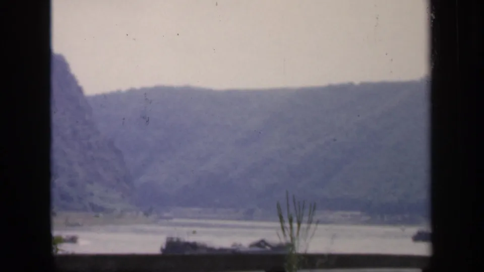 A soft 1949 Ireland home-movie view of distant hills and shoreline across water, framed by a dark window.