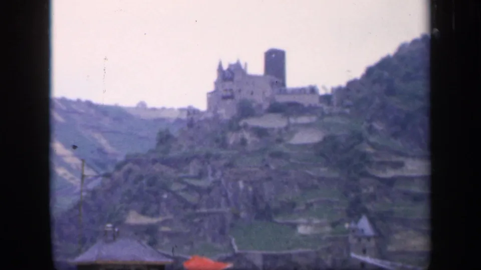 1949 Ireland frame with a castle-like hilltop structure, terraced slopes, rooftops, and dark window framing.