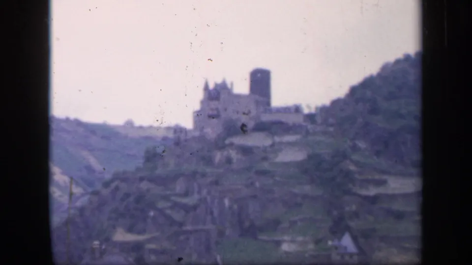 1949 Ireland home-movie frame showing a distant stone castle and tower on a hillside above terraced ground.