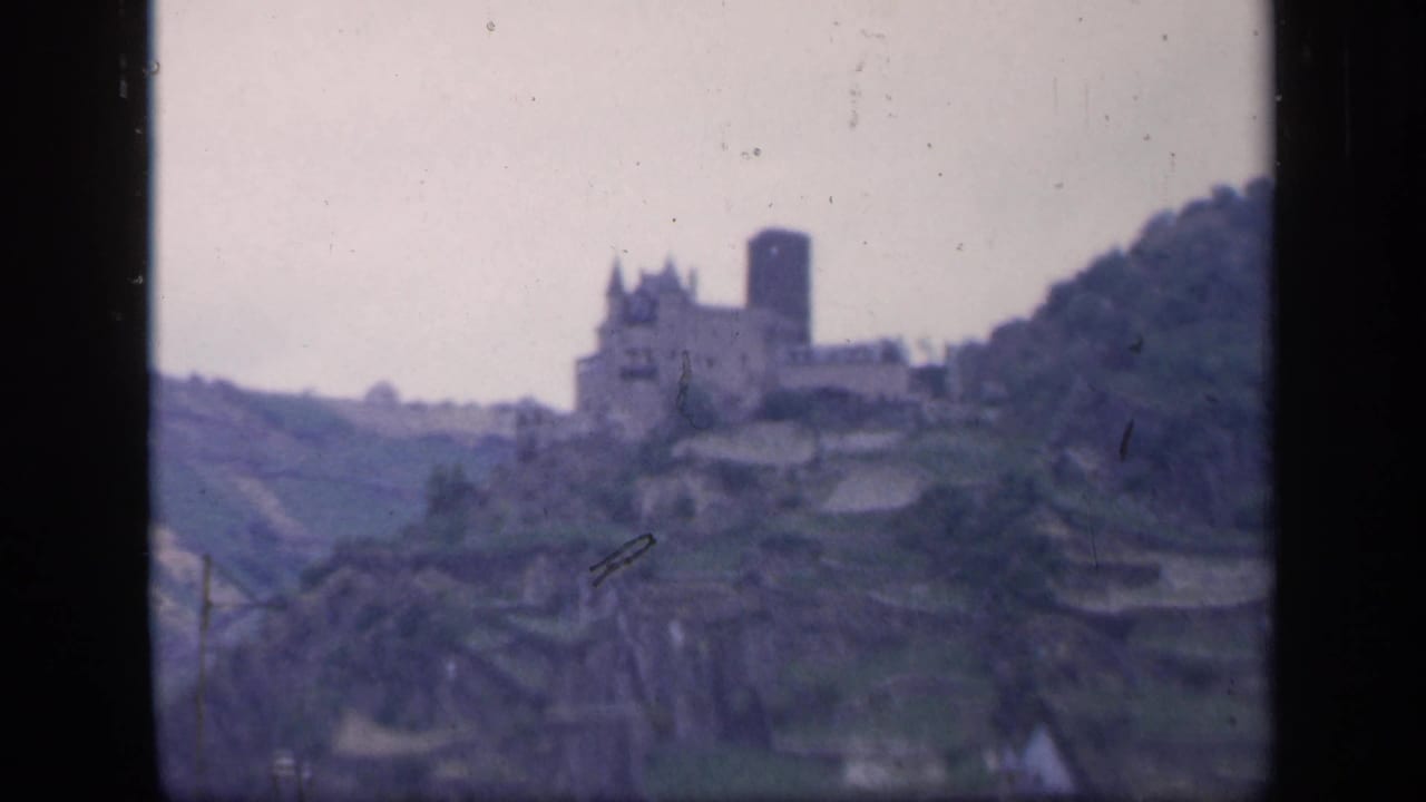 Distant castle and tower on a green hillside with film gate borders.