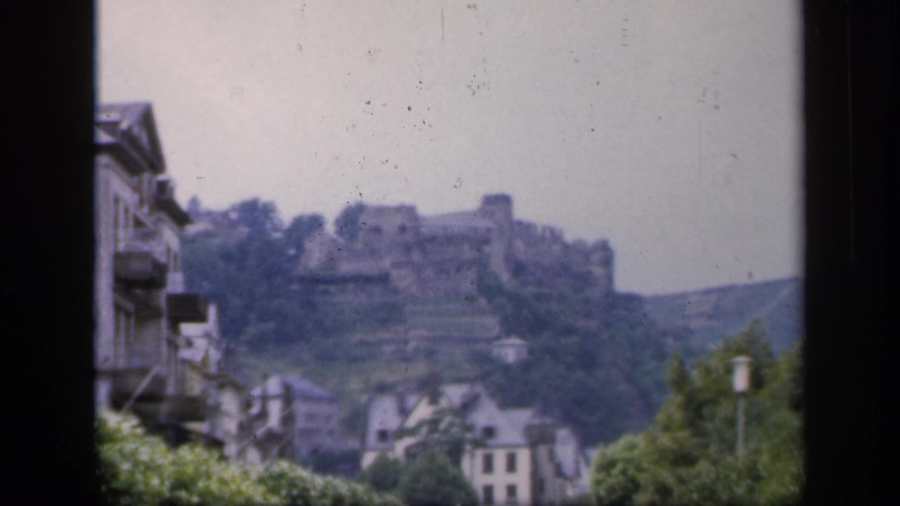 Distant hilltop castle ruin above town buildings, framed by dark window edges.