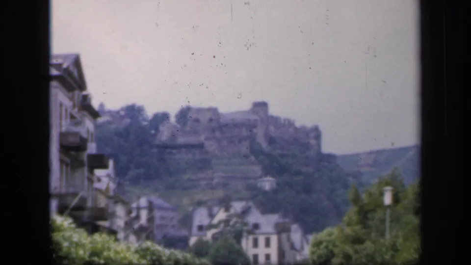 1949 8mm view in Ireland of a hilltop castle ruin above town rooftops, seen through a dark window frame.