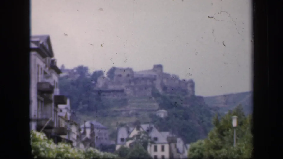 Ireland travel footage frame showing a distant castle ruin above buildings and trees, with visible 8mm grain.