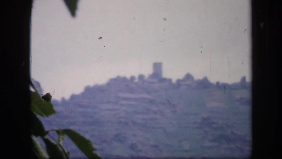 Final 1949 Irish 8mm frame with a distant hilltop tower or castle ruin, terraces, leaves, and window edge.