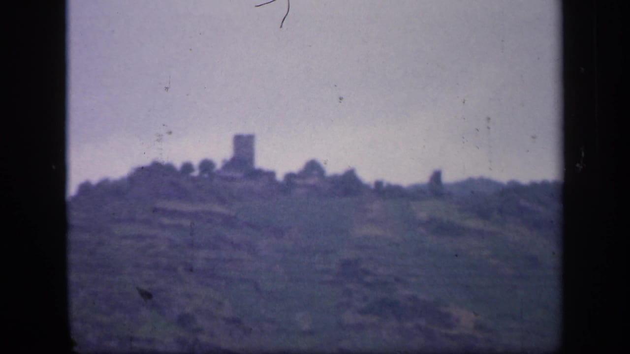 1949 Ireland 8mm frame with a soft-focus ridge, muted hills, and a distant stone tower or castle-like ruin.