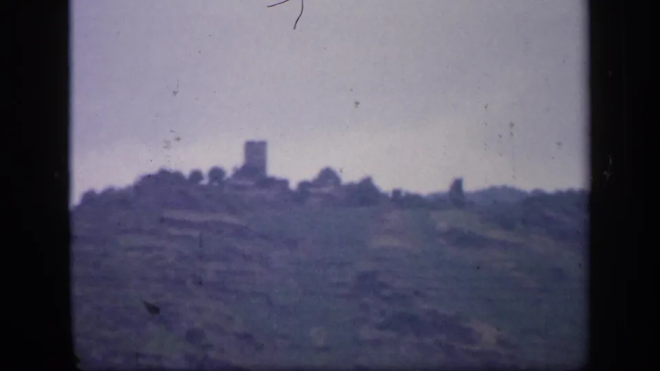 1949 Ireland 8mm frame with a soft-focus ridge, muted hills, and a distant stone tower or castle-like ruin.