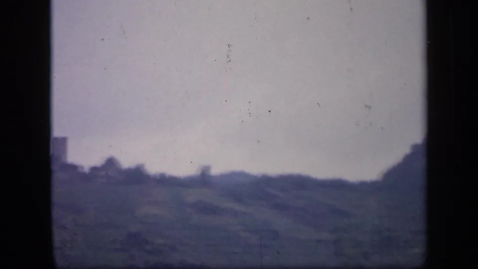1949 Ireland 8mm frame showing a misty rural hillside, pale sky, and a partial distant structure near the frame edge.