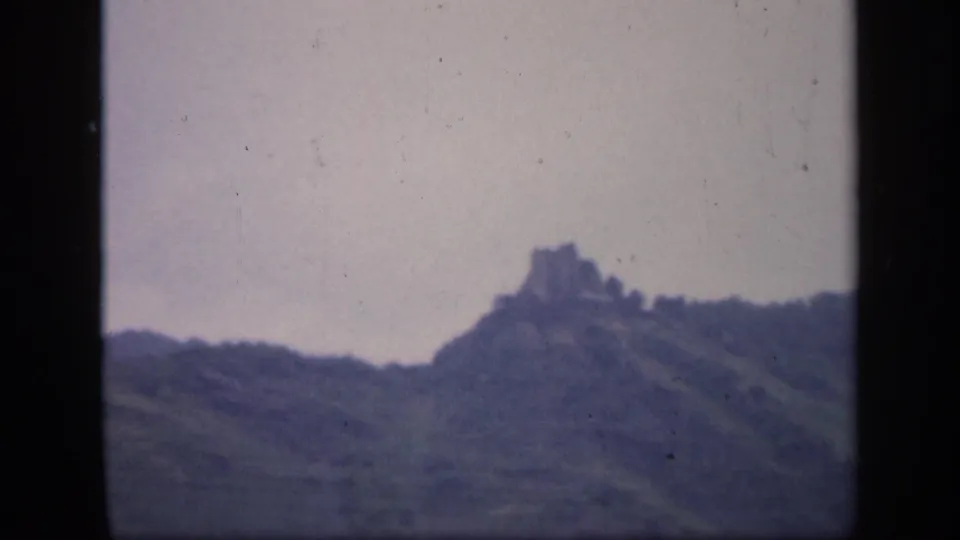 1949 Ireland 8mm frame showing a castle-like ruin on a hilltop ridge in a hazy rural landscape.
