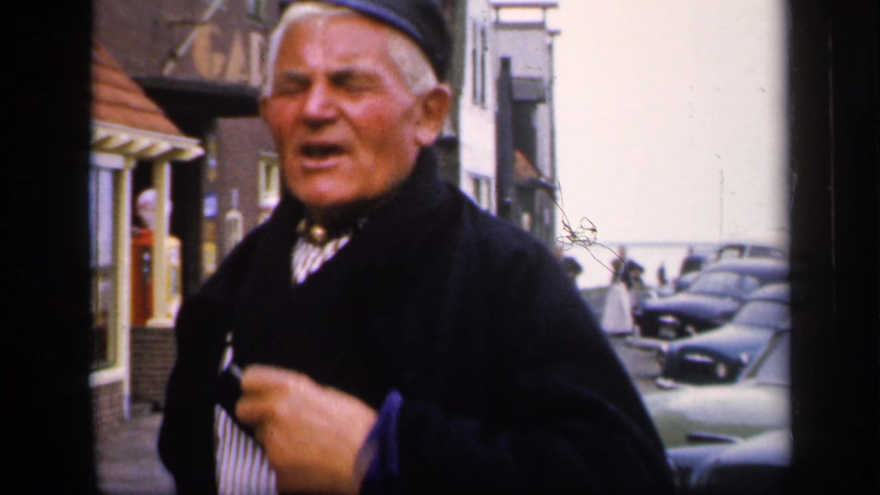 In 1949 Ireland footage, an elderly man in dark traditional-looking attire gestures while standing on a narrow town street.