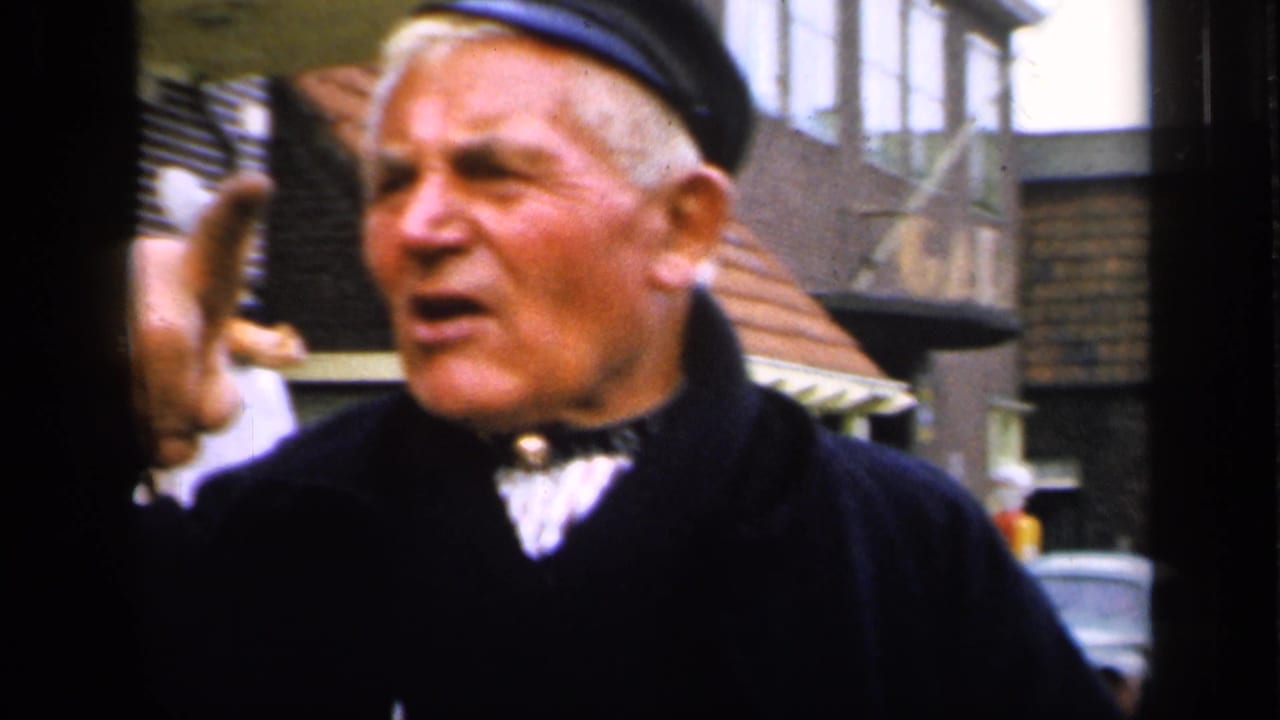 The elderly man in the 1949 Ireland clip raises a hand as if addressing the camera, with town buildings behind him.
