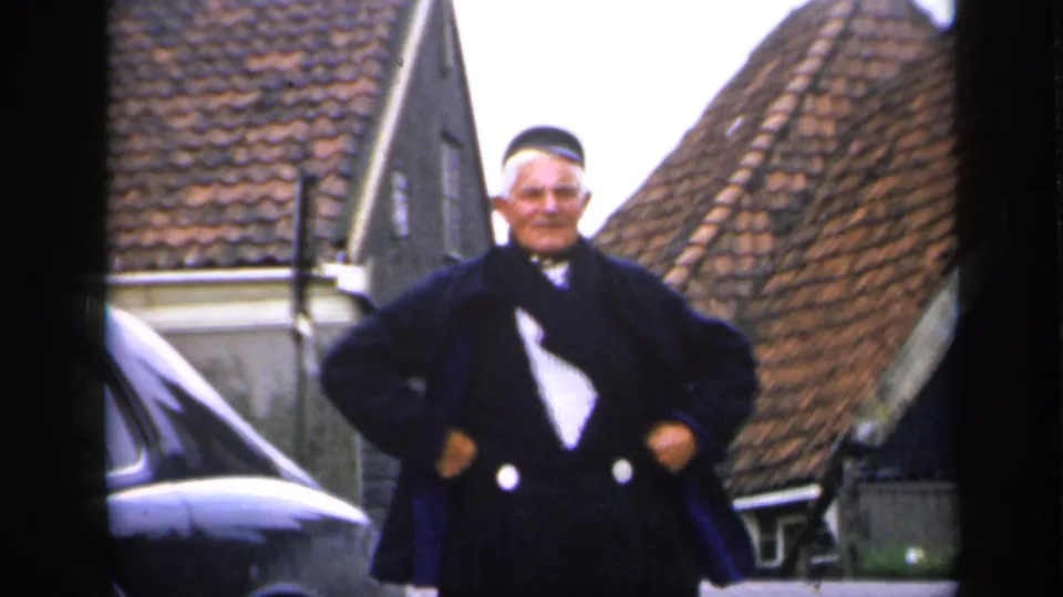 A wider 1949 Ireland frame shows the older man standing with hands at his waist near a car and tiled-roof buildings.