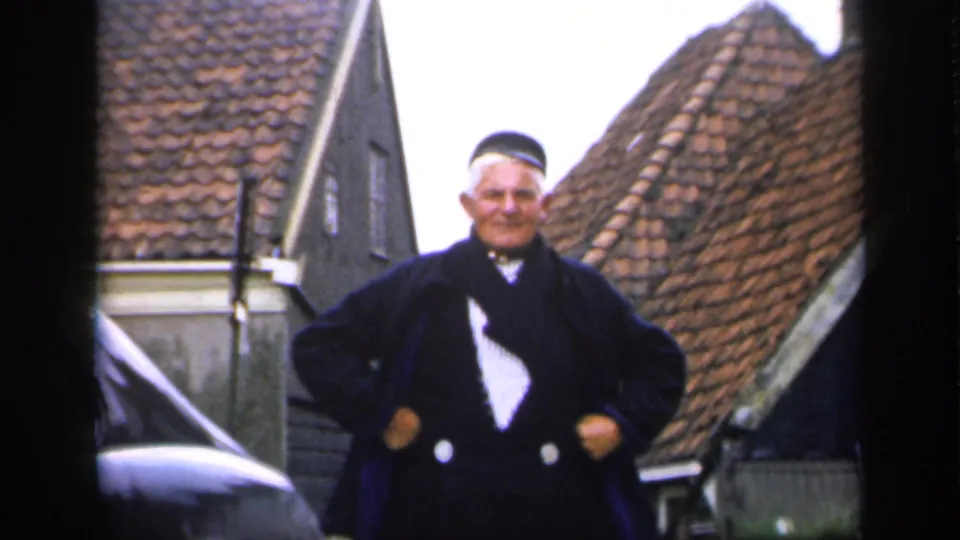 The 1949 Ireland home-movie view holds on the older man facing the camera, framed by cars and historic-looking rooflines.