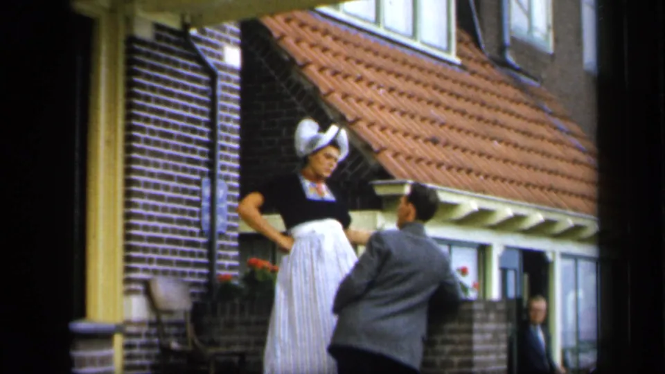 In Ireland 1949 footage, a bonneted woman outside a brick house turns toward a man in a gray suit.