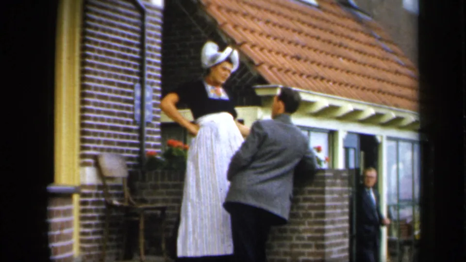 In Ireland 1949 footage, a suited man faces a woman in bonnet and apron outside a residential brick facade.