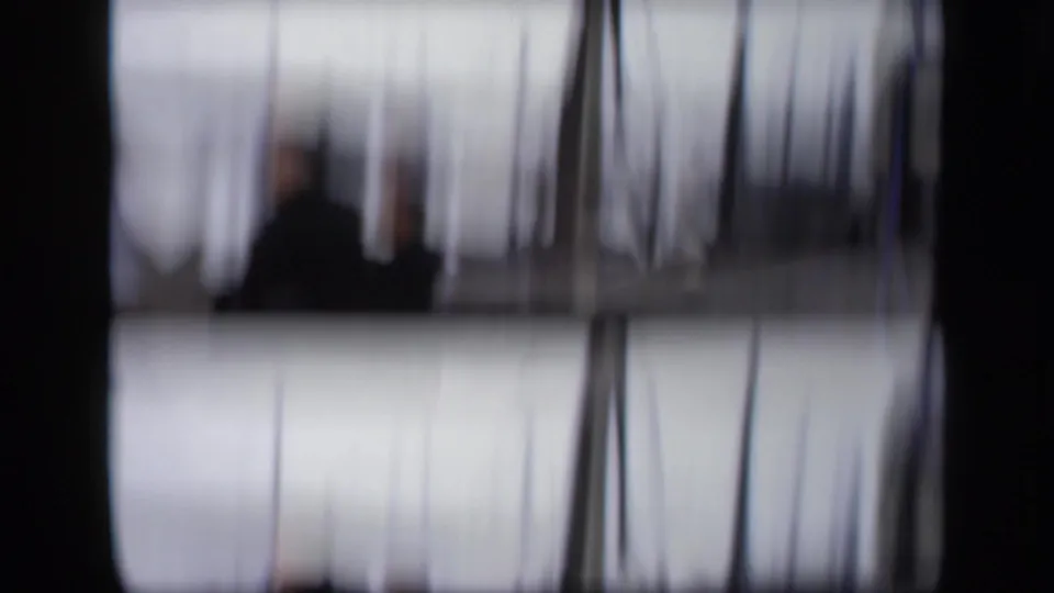 A soft 8mm frame shows blurred vertical masts or window lines with a dark figure shape near the center.