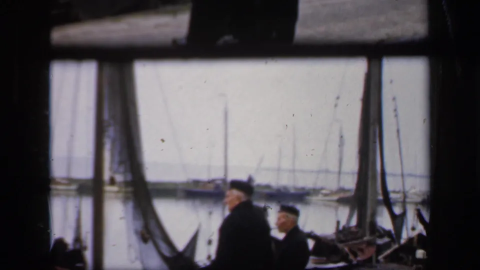 The 1949 Ireland harbor view shows two men partly low in frame, with sailboat masts and calm water in the background.
