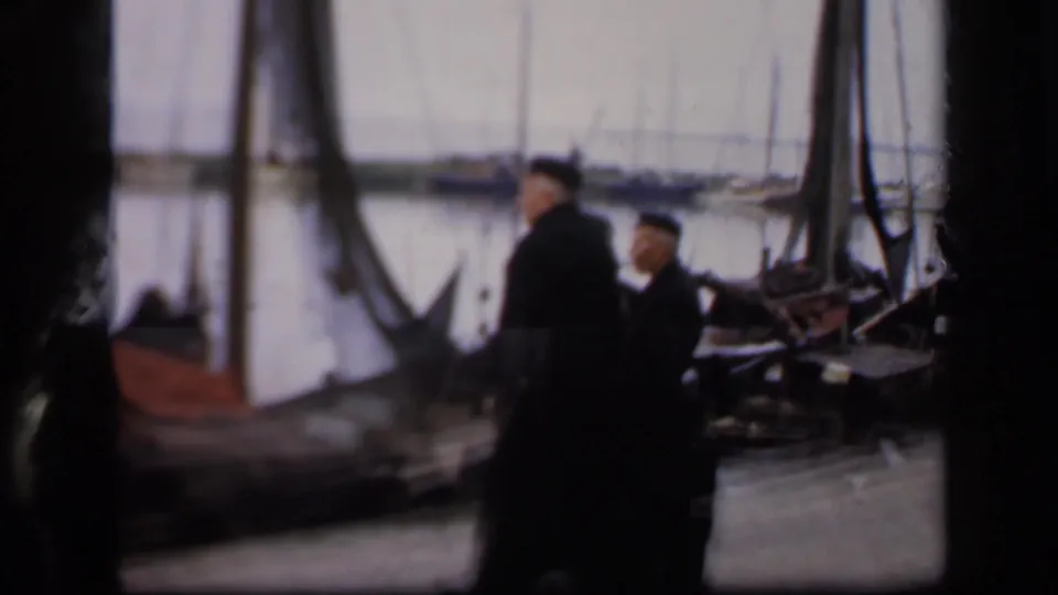 In the clearest frame, two men in dark coats and caps stand near moored boats on a 1949 Ireland harbor scene.