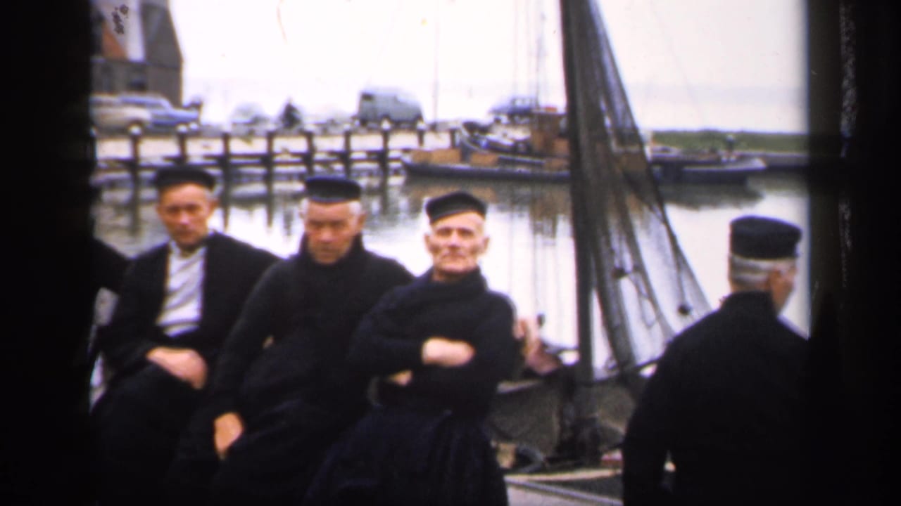 Seated men on a dock with another man turned away at the right edge.