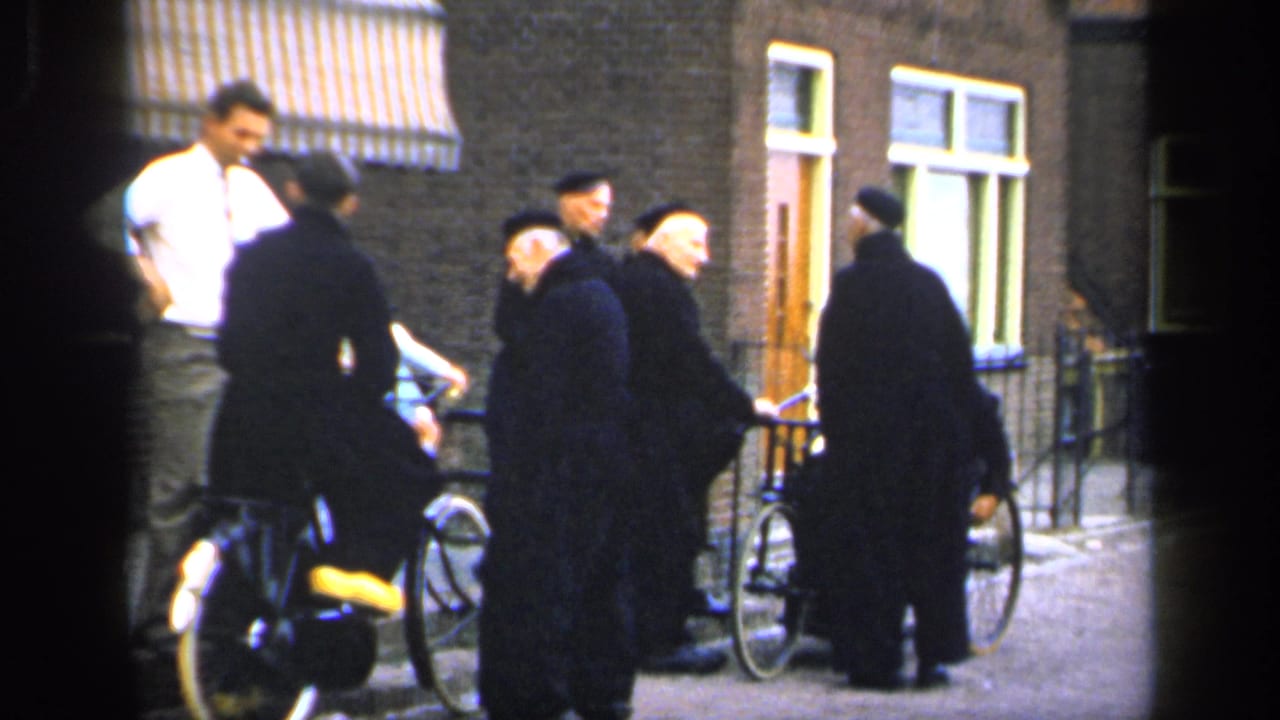 Men in dark clothing stand with bicycles while a younger man in a white shirt stands nearby.