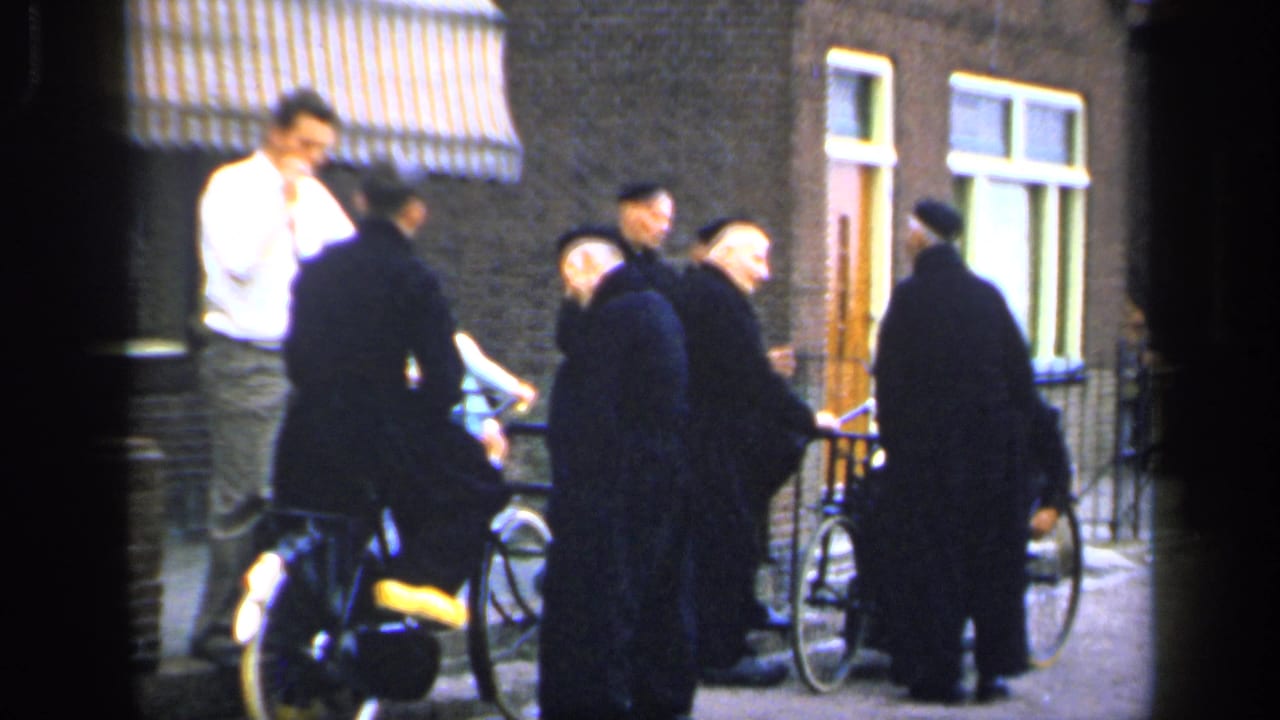 Group of men with bicycles talk outside a brick building with windows and a striped awning.