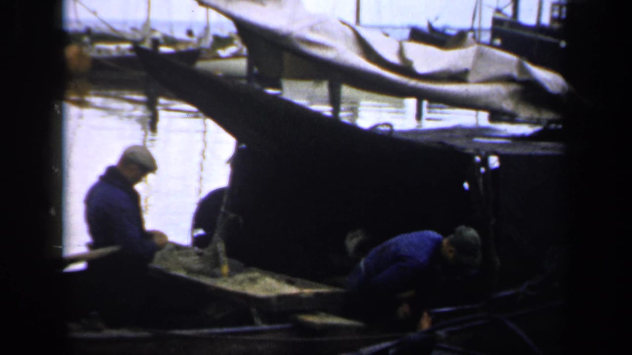 Two men in blue work clothes on a small boat at a harbor.