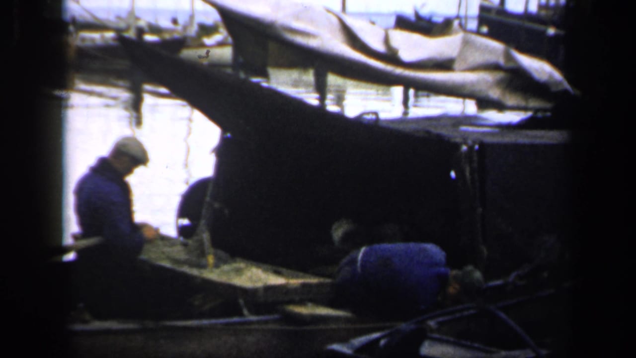 One man sits while another bends over inside a harbor boat.