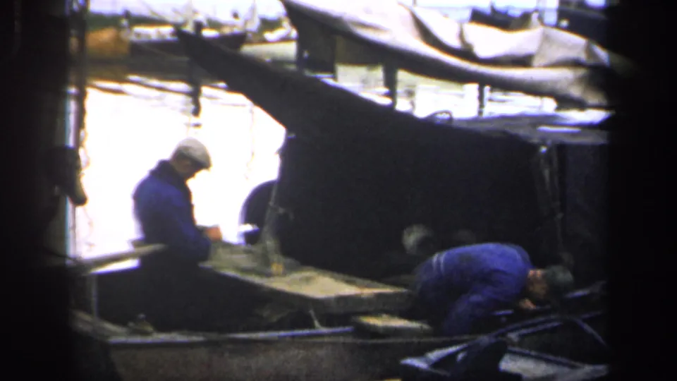 In 1949 Ireland footage, two men in blue work clothes appear to clean or tend a small fishing boat at a dock.
