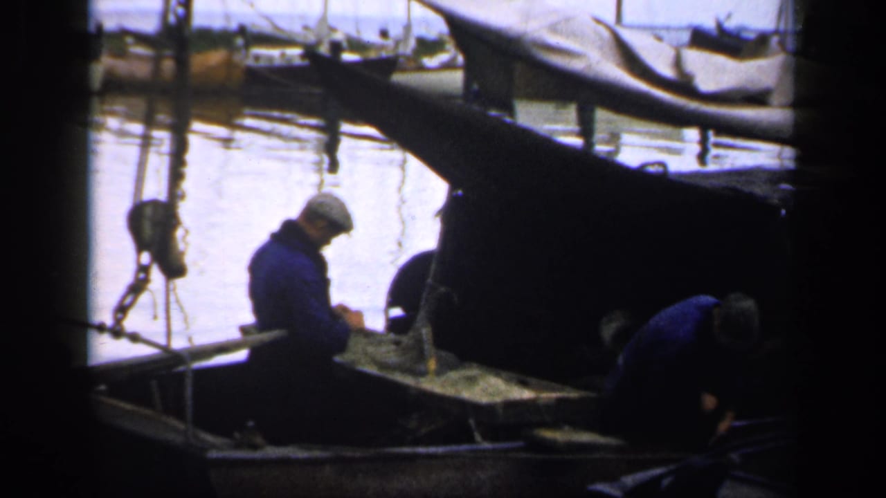 Two men continue working in a small boat near covered boats on the water.
