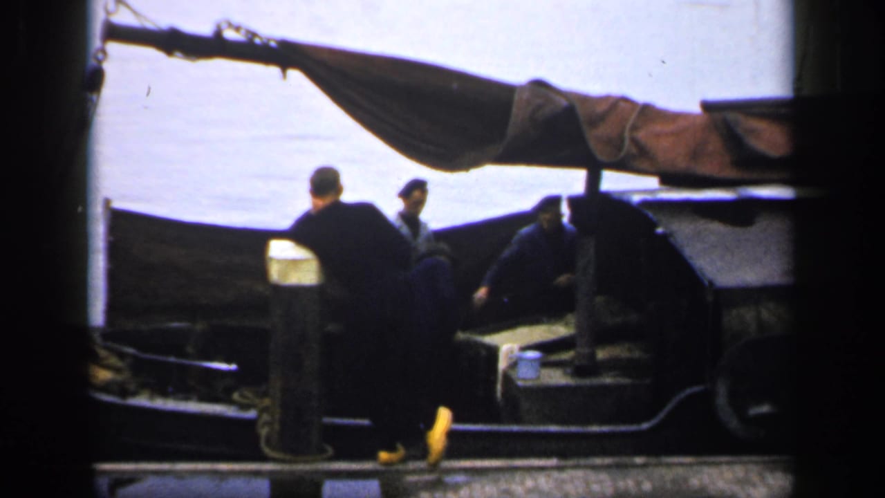 Three men around a small boat at a dock, with water behind them.