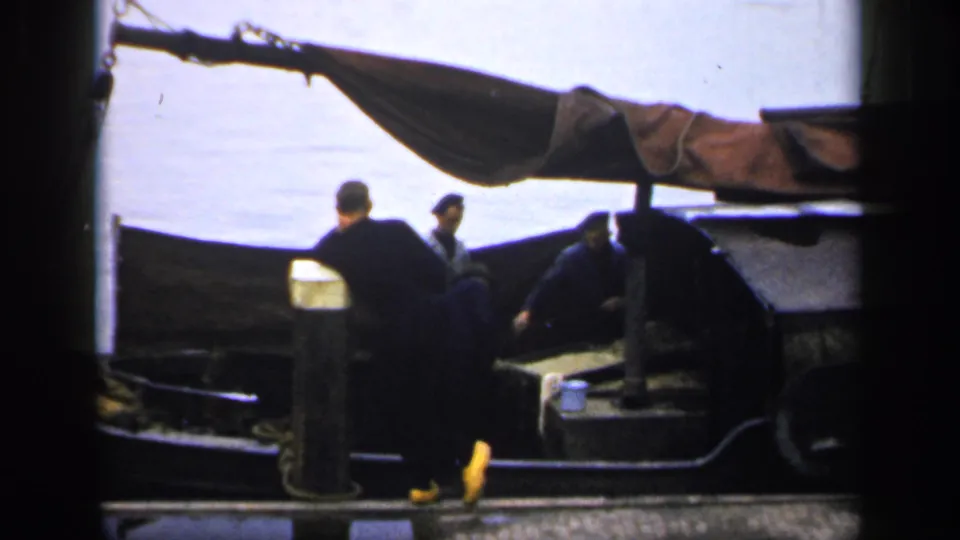 1949 Ireland 8mm frame showing one man on the dock and two men aboard a small boat under a canvas awning.
