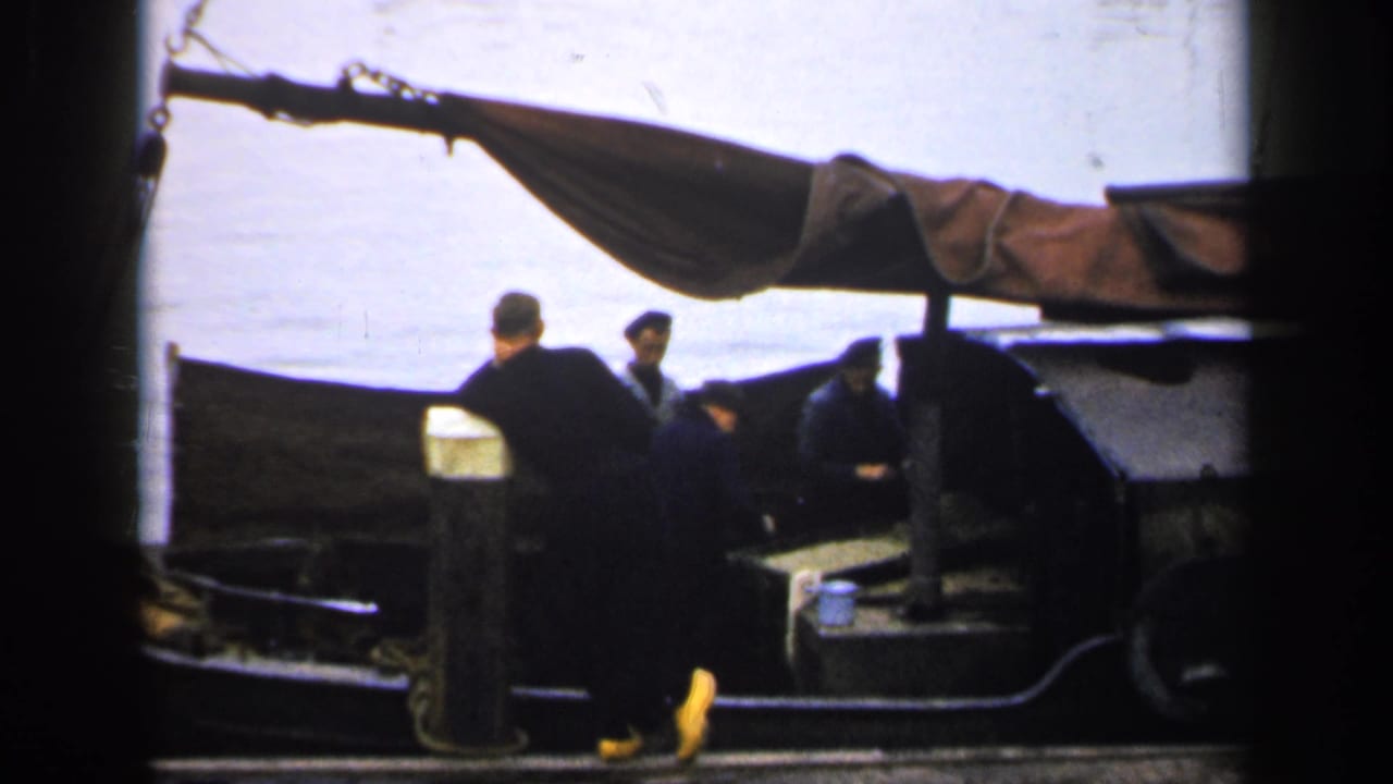1949 Ireland 8mm frame with a dockside man facing two men seated in a small covered boat by the water.