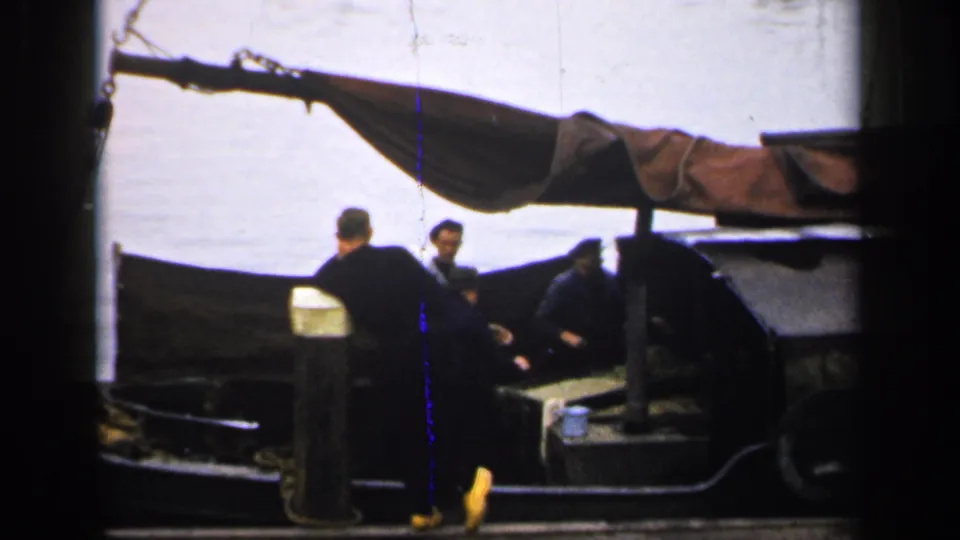 1949 Ireland 8mm frame showing three men beside and inside a small boat, partly obscured by a foreground dock post.