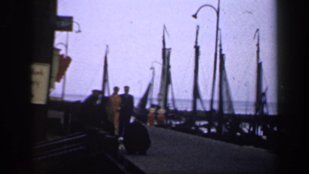 Couple walking along a dock beside moored sailboats and tall masts.