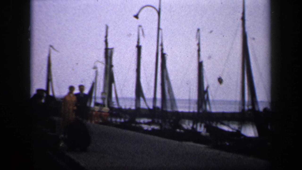 Silhouetted adults on a pier with sailboat masts and lampposts behind them.