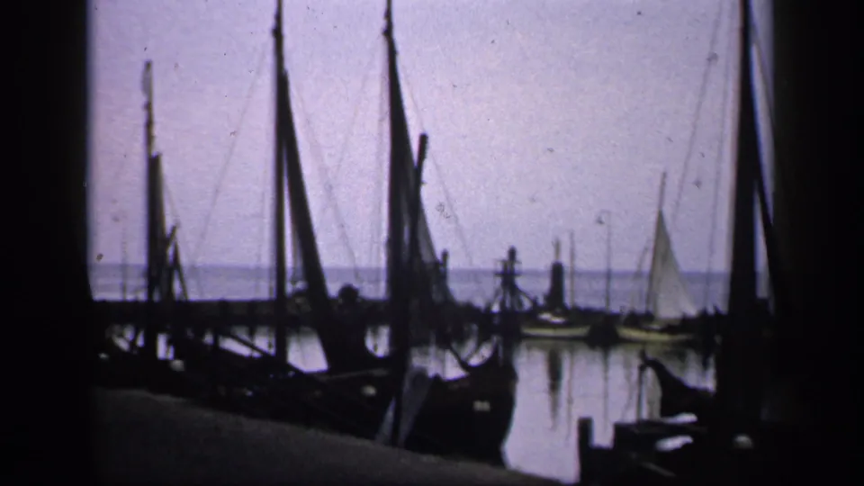 1949 Ireland 8mm frame showing moored sailboats, rigging, dock edges, and calm water under a pale sky.