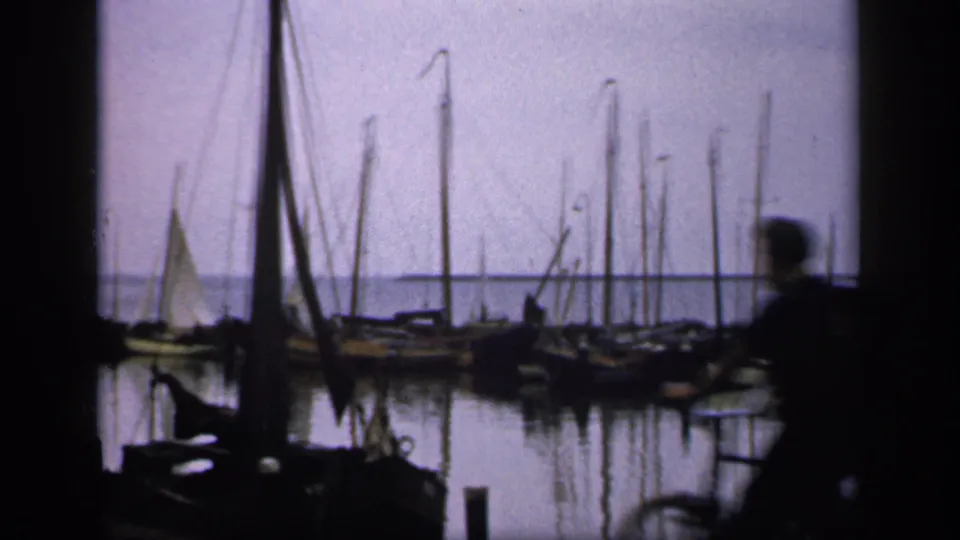 1949 Ireland harbor frame with moored boats and masts, while a dark blurred passerby crosses the foreground.