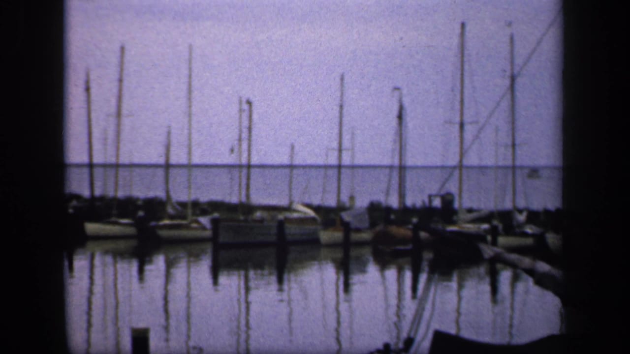 Sailboats moored along a marina with still water and mast reflections.