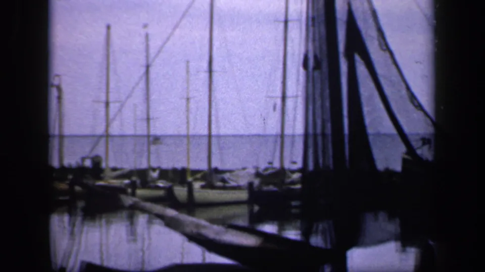 1949 Ireland marina frame with dark foreground rigging, a dock edge, moored sailboats, and still water reflections.